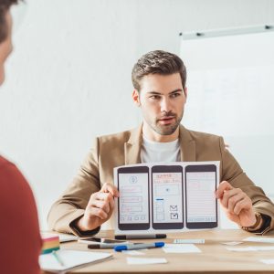 Selective focus of designer showing layout of mobile web prototype to colleagues in office