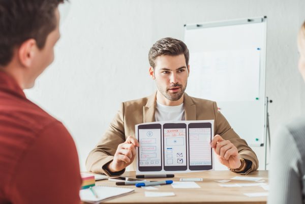 Selective focus of designer showing layout of mobile web prototype to colleagues in office