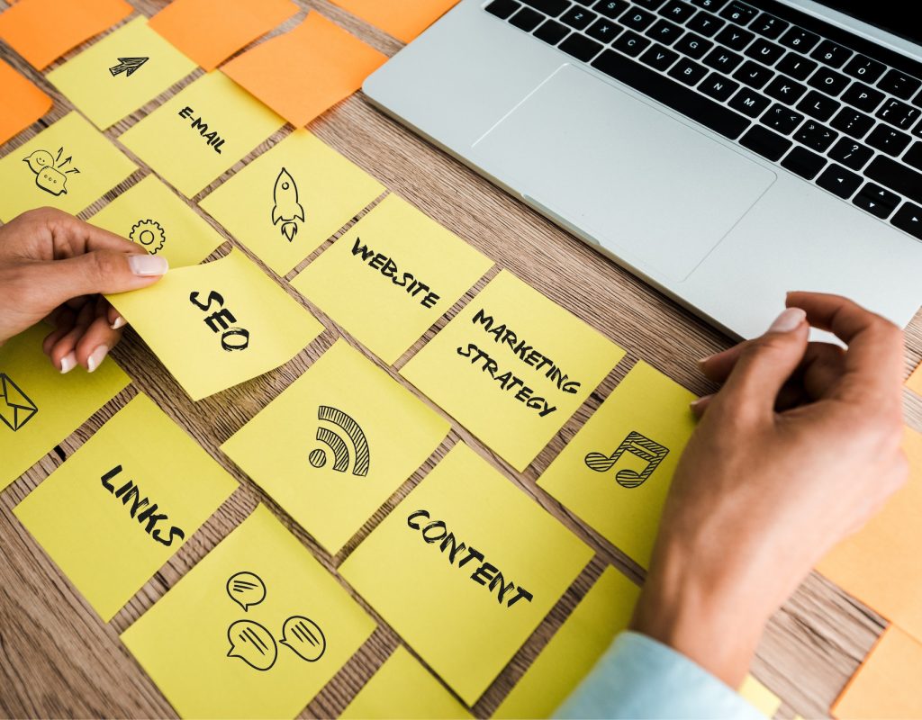 cropped view of woman touching sticky note with seo lettering near laptop on desk