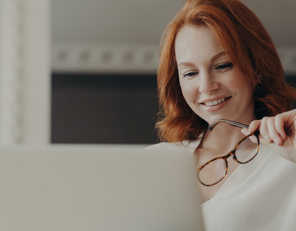 Good looking cheerful redhead woman reads information on website in internet