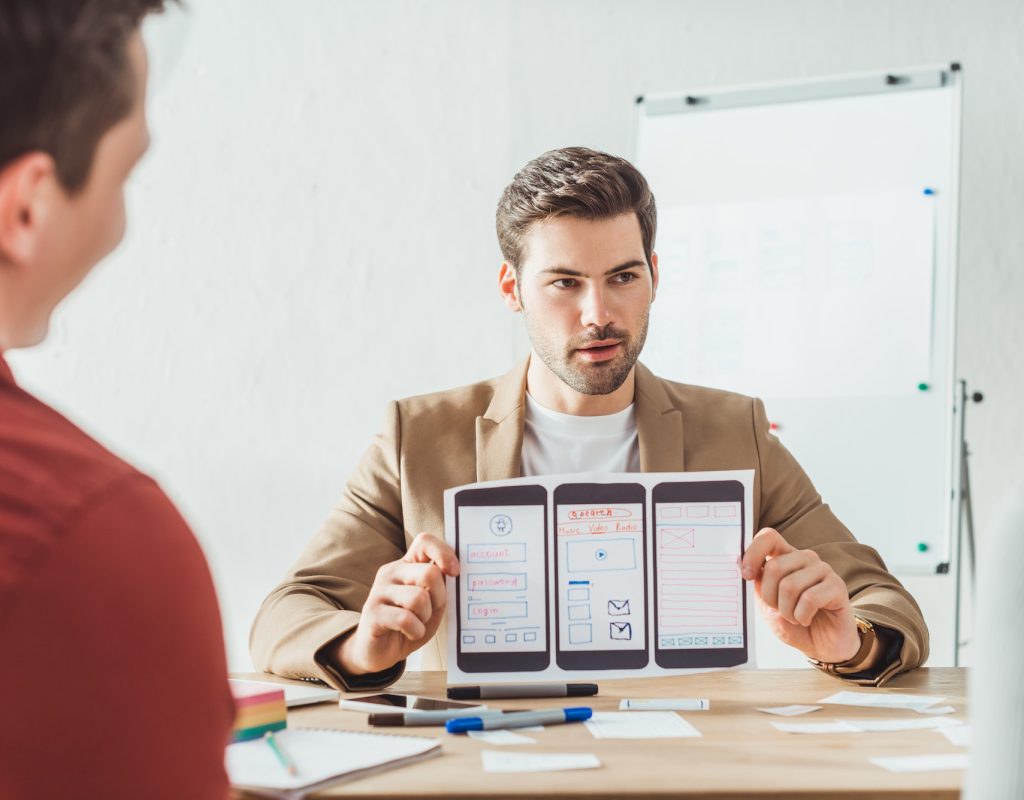 Selective focus of designer showing layout of mobile web prototype to colleagues in office