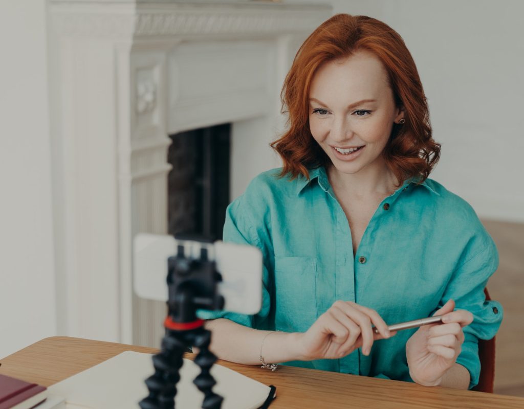 Social media influencer blogger keeps mobile phone on tripod, looks gladfully at camera