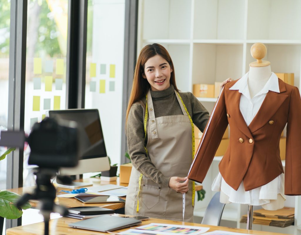 Young Asia lady fashion designer using mobile phone receiving purchase order and showing clothes re